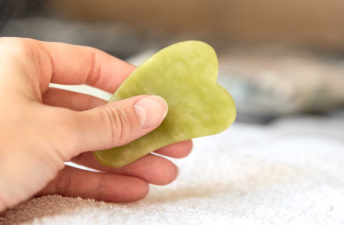 Female hand holding green gua sha facial massager