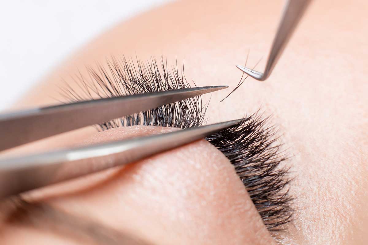 Eyelash extension procedure. Master tweezers sets fake lashes on beautiful woman.