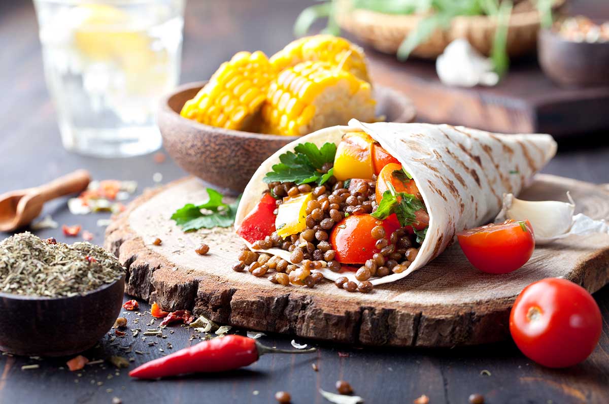 Vegan tortilla wrap, roll with grilled vegetabes and lentil and boiled corn cob on a wooden background