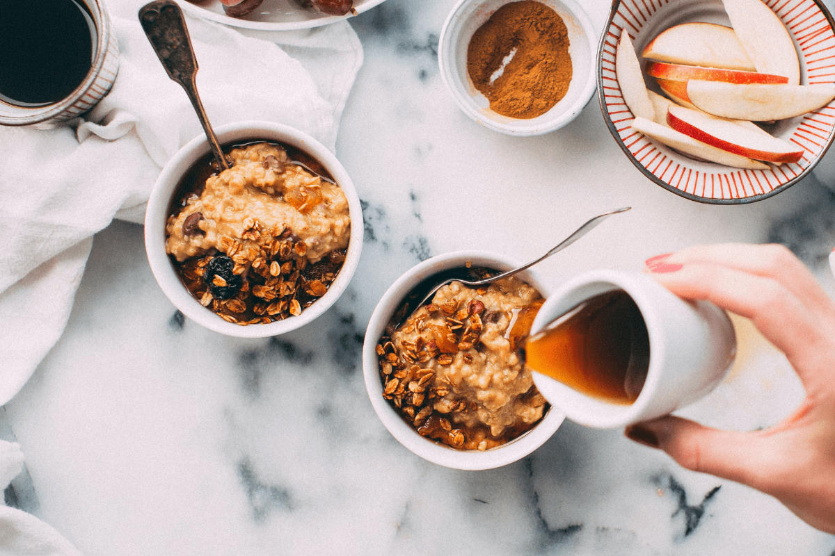 maple syrup poured onto oatmeal bowls with apple slices - healthy morning breakfast