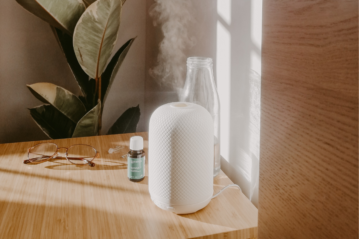 essential oil diffuser in sunlight on a wooden table with plant in background
