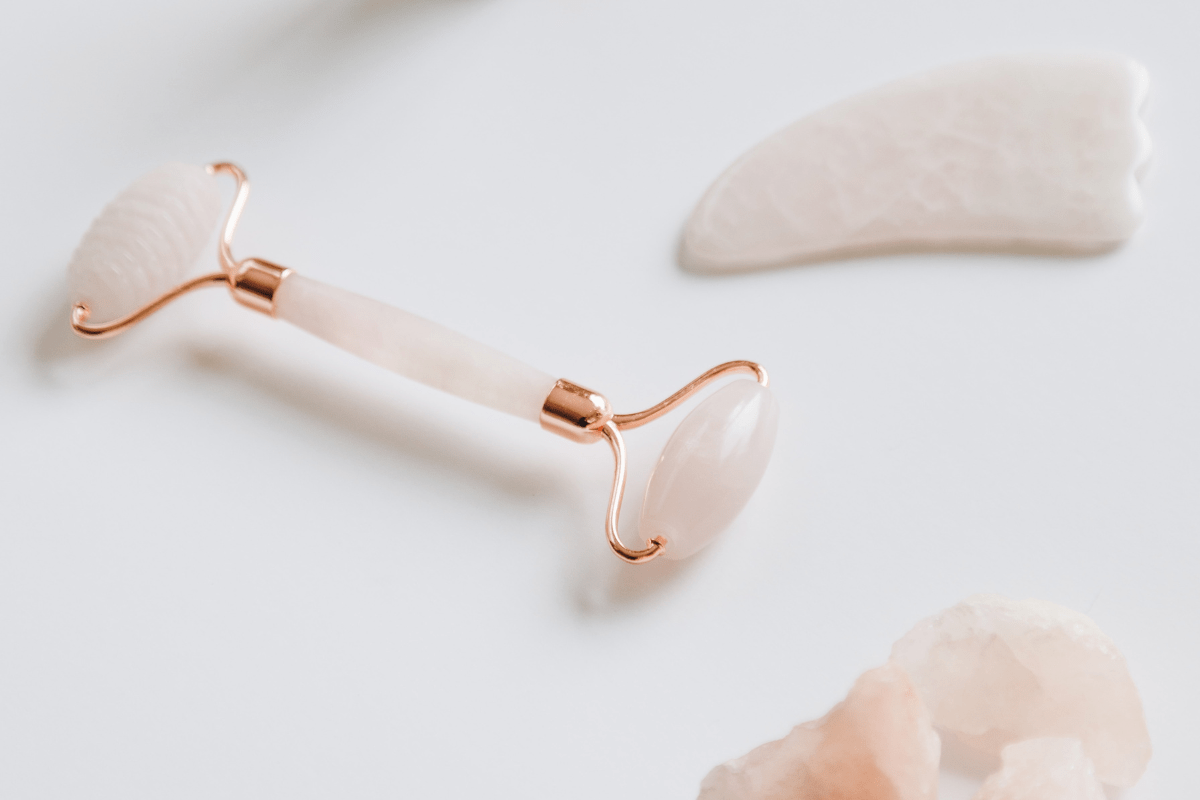 rose quartz pink gua sha and face roller lying on white table