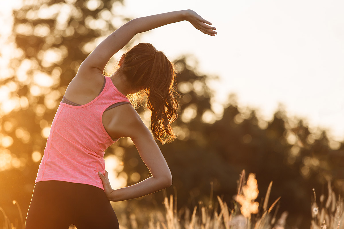 Young female workout before fitness training session at the park. Healthy young woman warming up outdoors. She is stretching her arms and looking away,hi key.