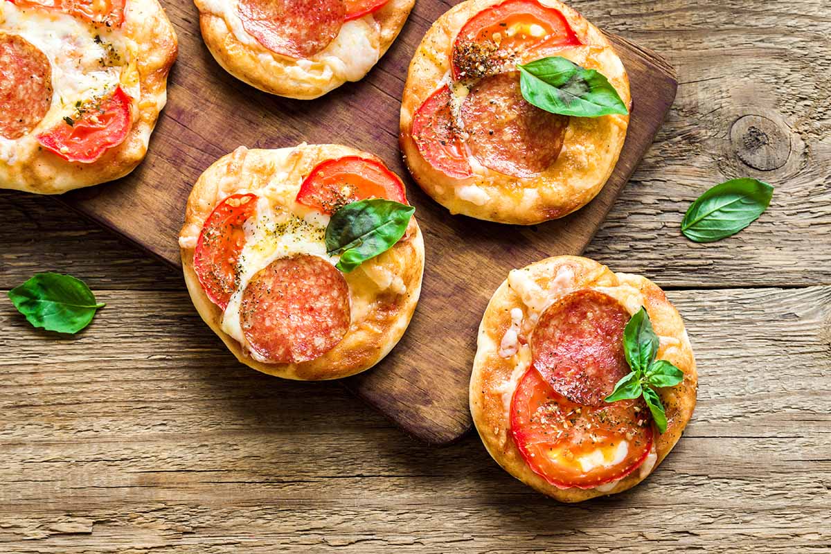 Mini Pizzas - Fresh homemade mini pizzas with pepperoni, cheese, tomatoes and basil on rustic wooden background with copy space.