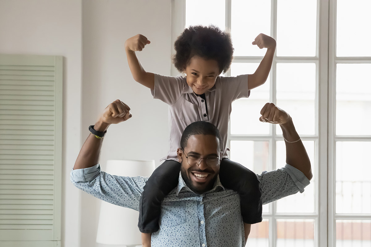 Small son sit on strong dad shoulders showing biceps. African family enjoy activity games at home, healthy fit lifestyle, two superheroes, vitamins for adults and children ad, happy Father Day concept