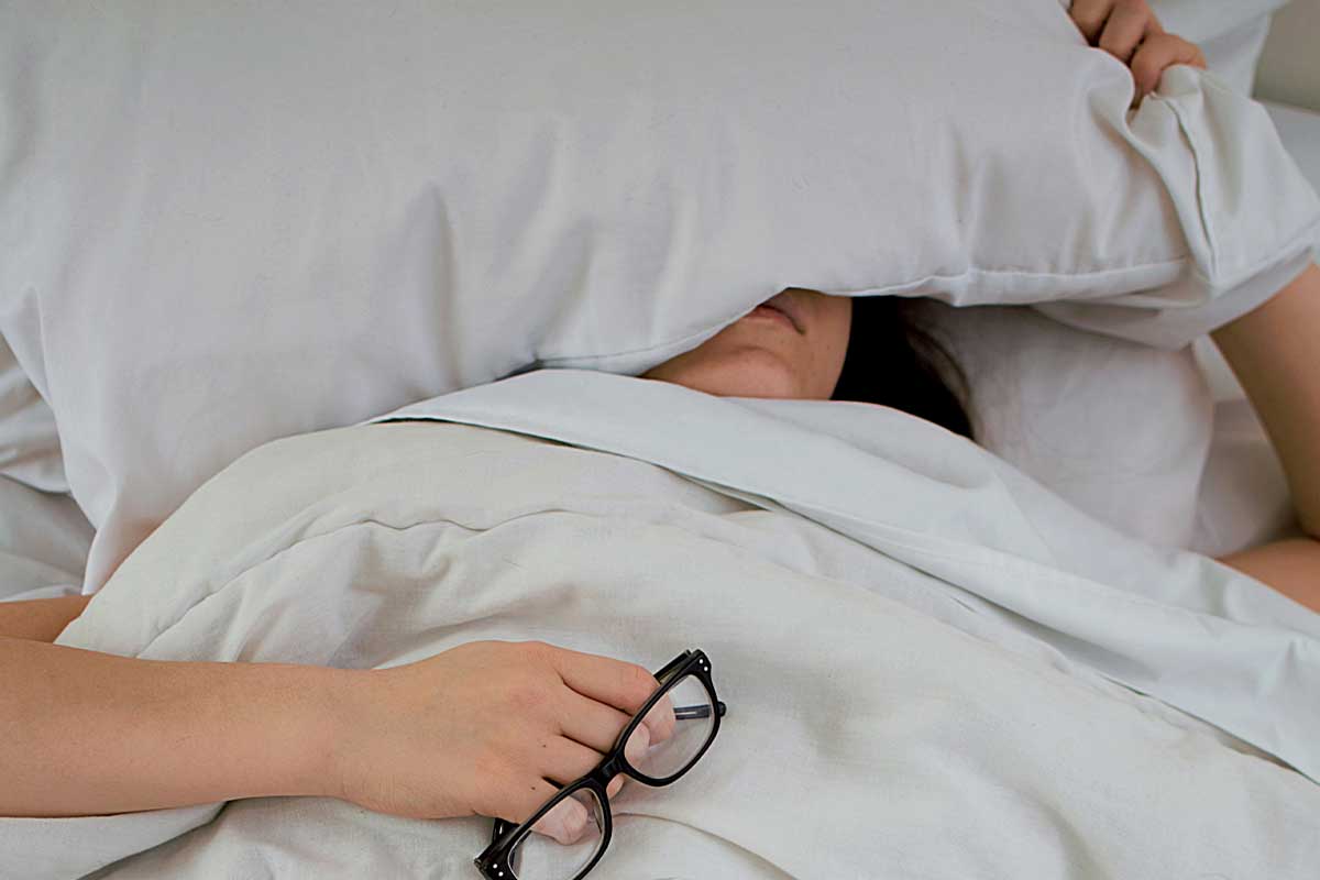 Woman sleeping under a pillow in bed